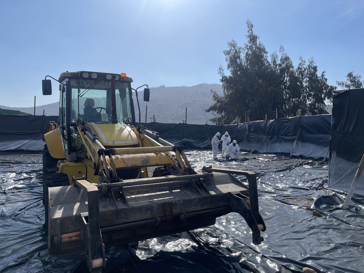Terreno de basural controlado con geomembrana, maquinaria y cuadrilla EPP durante el saneamiento